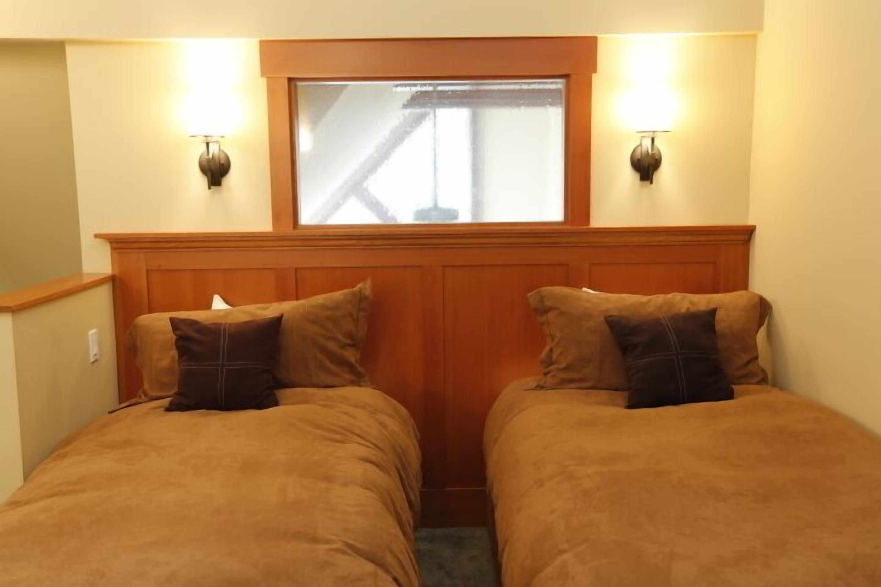 Une chambre avec deux lits, une tête de lit en bois, une fenêtre et des lampes fixées au mur.