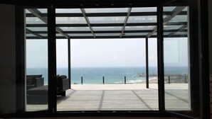 A modern room with a large sliding glass door leading to a balcony with a view of the ocean.