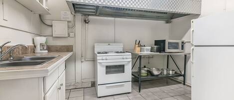 A compact kitchen with a white stove, oven, and microwave. There is a sink with a faucet, a countertop, and a shelf with kitchen utensils.