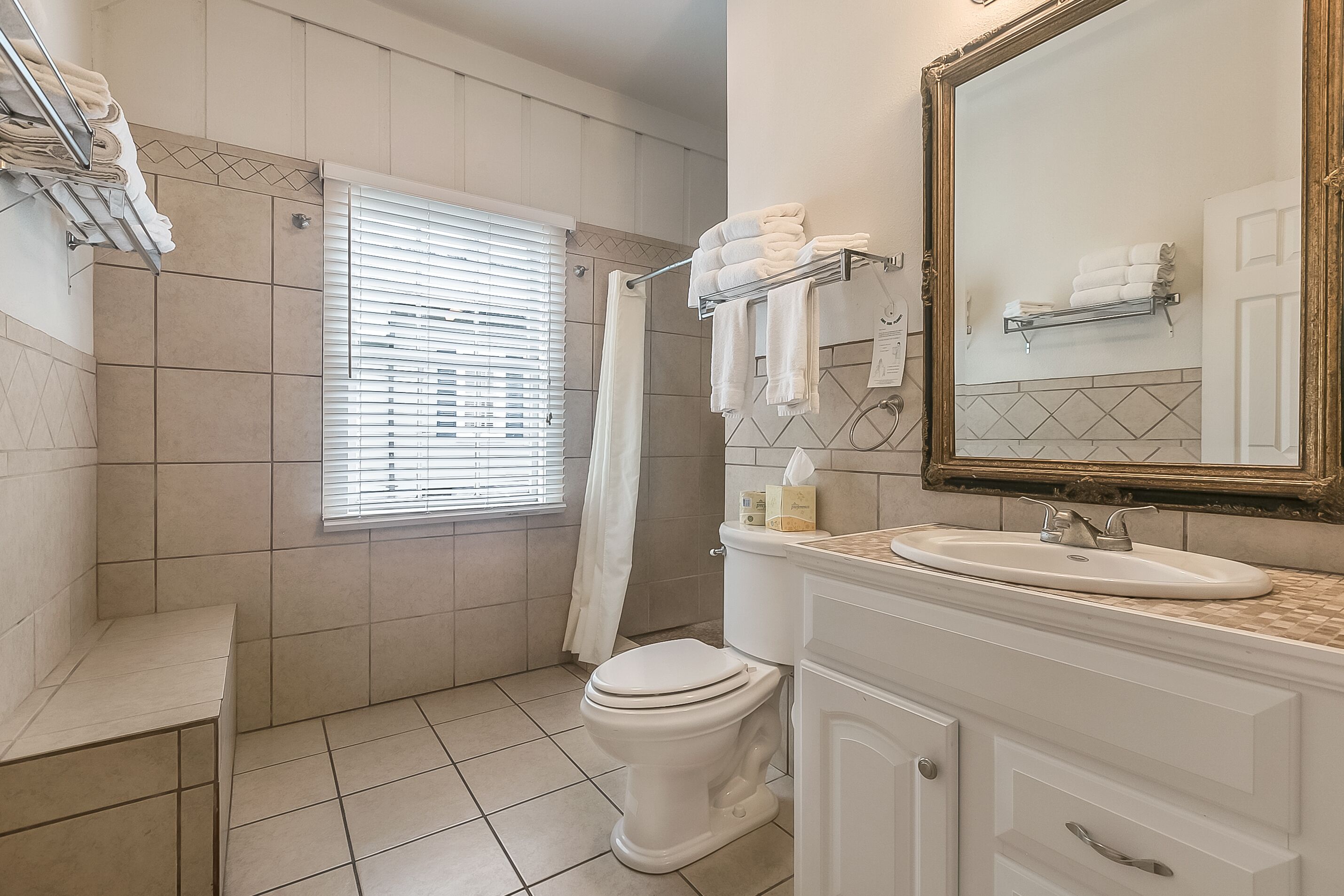A bathroom with a toilet, sink, and mirror. There are towels on a rack and a shower curtain.