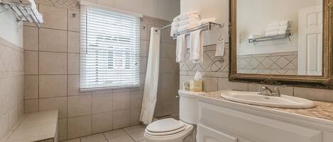 A bathroom with a toilet, sink, and mirror. There are towels on a rack and a shower curtain.