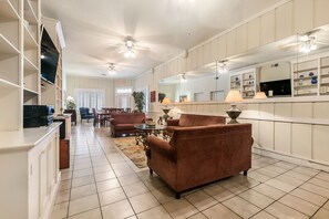 A spacious living room with a large sofa, a coffee table, and a TV mounted on the wall. There are ceiling fans and a large mirror above the sofa. - Prime Location, 3 Blocks to Bourbon St. A great space for groups to enjoy NOLA. (New Orleans)
