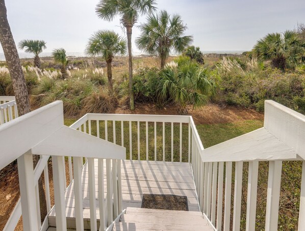 A wooden staircase leading to a deck with white railings, surrounded by palm trees and beach vegetation.