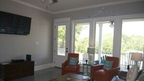 Una sala de estar con televisor, una mesa de centro, un sofá y dos sillones. Un letrero sobre la puerta dice: BIENVENIDOS AL LAGO.