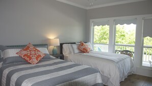 Un dormitorio con dos camas, una mesita de noche con lámpara y ventanas amplias con vistas al verdor.