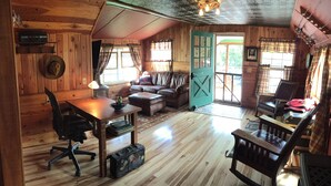 Interior acolhedor de uma cabana, com decoração em madeira, um sofá de couro, uma mesa de jantar e uma escrivaninha com cadeira.