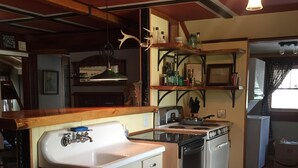 Cozinha compacta com pia, fogão e lava-louças. Há prateleiras de madeira acima do balcão e um ventilador de teto.