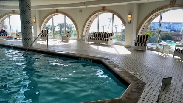 A pool area with a 6-foot depth warning, lounge chairs, and large arched windows offering views of palm trees and a pool. - GREAT GALVESTON GETAWAY! STRESS-FREE BEACH VACATION! (Galveston)