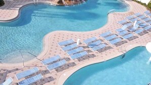 Een zwembad met een golvend ontwerp, omgeven door een zandstrand met rijen ligbedden en parasols.