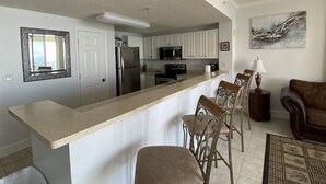Een moderne keuken met witte kasten, een roestvrijstalen koelkast en een bar voorzien van metalen stoelen.
