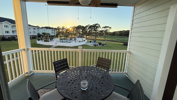 A covered outdoor patio with a table and chairs, overlooking a golf course and residential buildings. - 5 minutes to the beach! Cozy 2 King BR 2BA Condo at Myrtlewood Golf Club (Myrtle Beach)