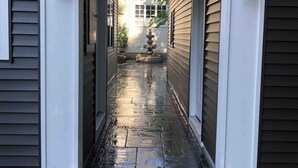 A narrow, wet stone pathway leading to a house entrance with a decorative fountain and two wall-mounted lanterns. - Lake Michigan Beach & Heated Pool 1 King  BR+  Cottage Sleeps 3 (South Haven)