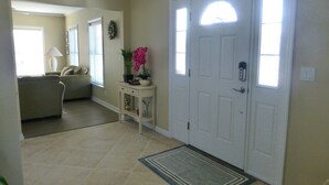 A hallway with a white door, a small console table with decorative items, a patterned rug, and a living room area with a couch and a lamp. - 2 min walk to Jenkinson's Beach/Boardwalk. Beautiful, large house for big family (Point Pleasant Beach)