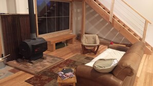 Een gezellige woonkamer met een open haard, een bank, een fauteuil en een houten trap.