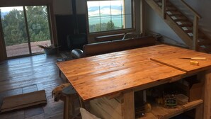 Een ruime kamer met een grote houten tafel, een hond en uitzicht op de omgeving door een groot raam.