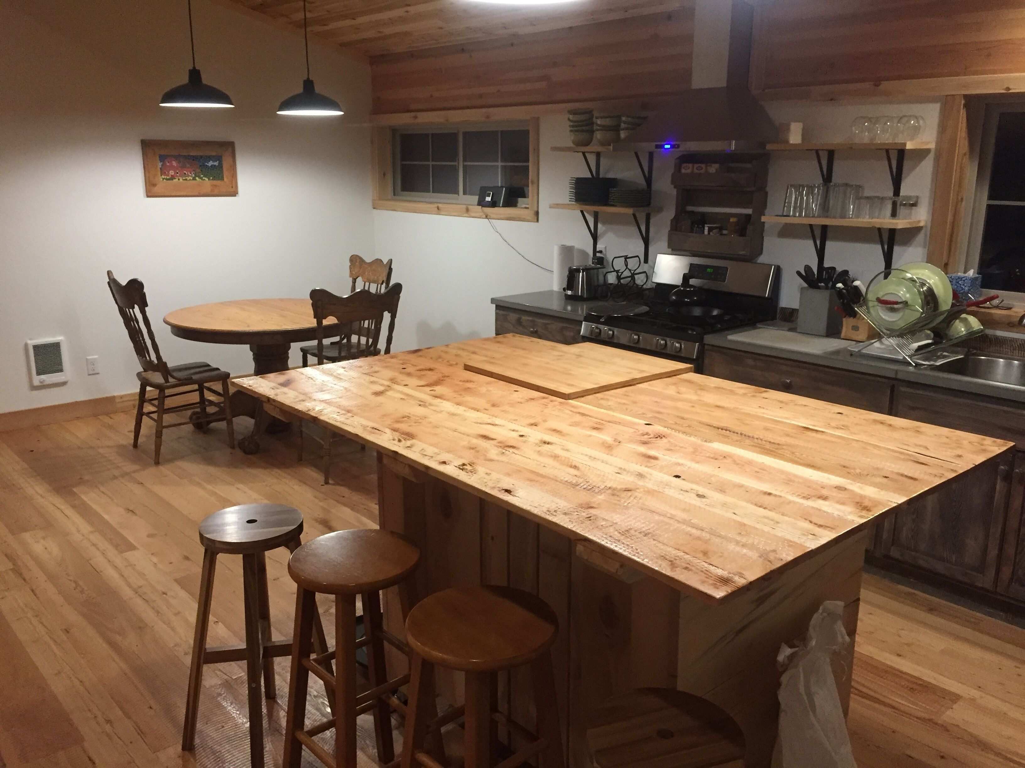 Une cuisine dotée d’un îlot central, de chaises en bois, d’une table à manger et d’un luminaire suspendu.