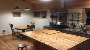 Een keuken met een centraal eiland, houten stoelen, een eettafel en een hanglamp.