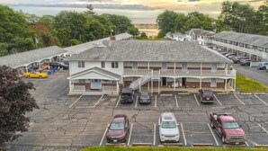 Un motel composé d’un bâtiment principal et de plusieurs unités attenantes, avec un parking où sont stationnées plusieurs voitures.