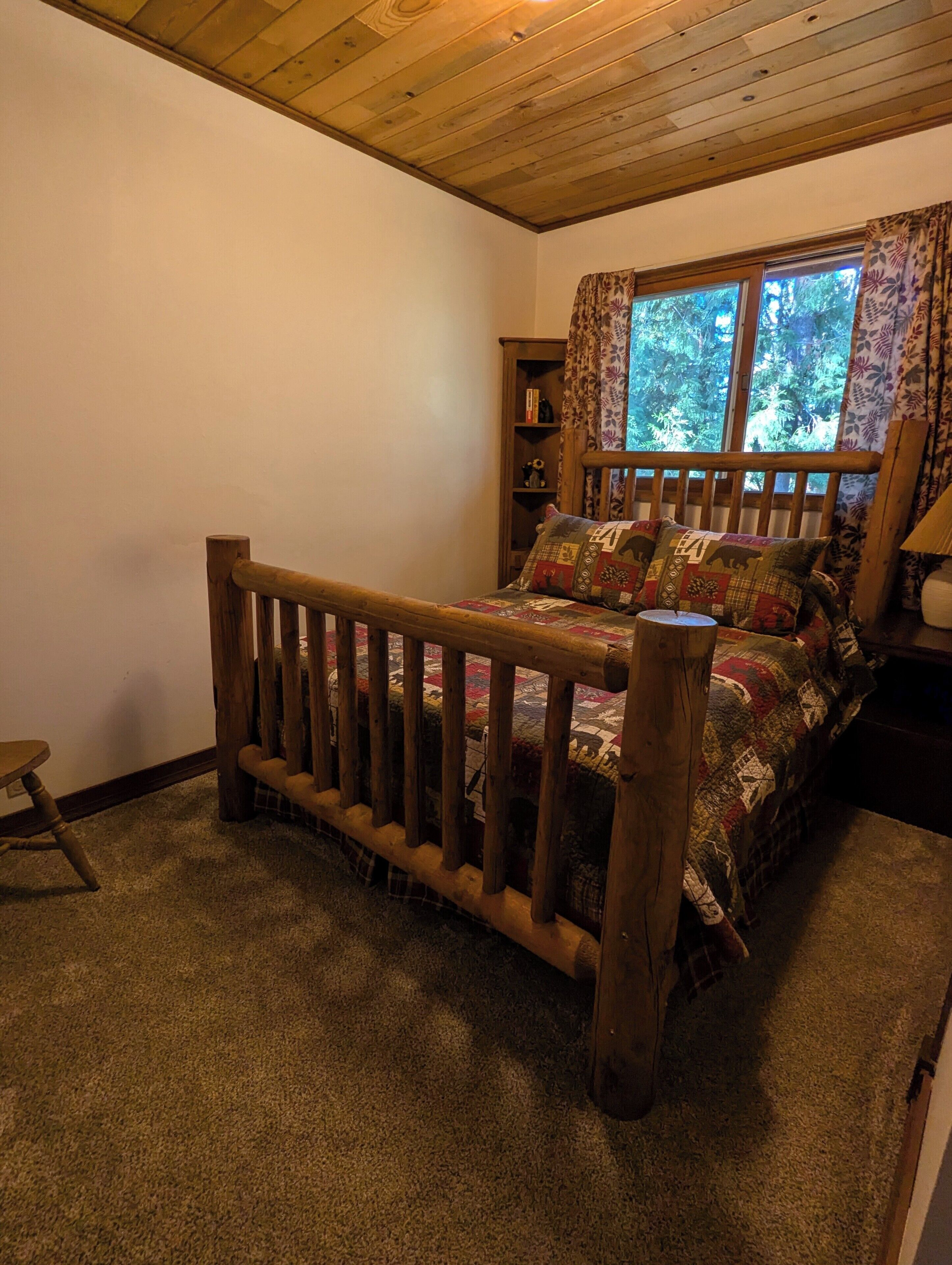 A cozy bedroom with a wooden bed, a bookshelf, and a window with curtains.