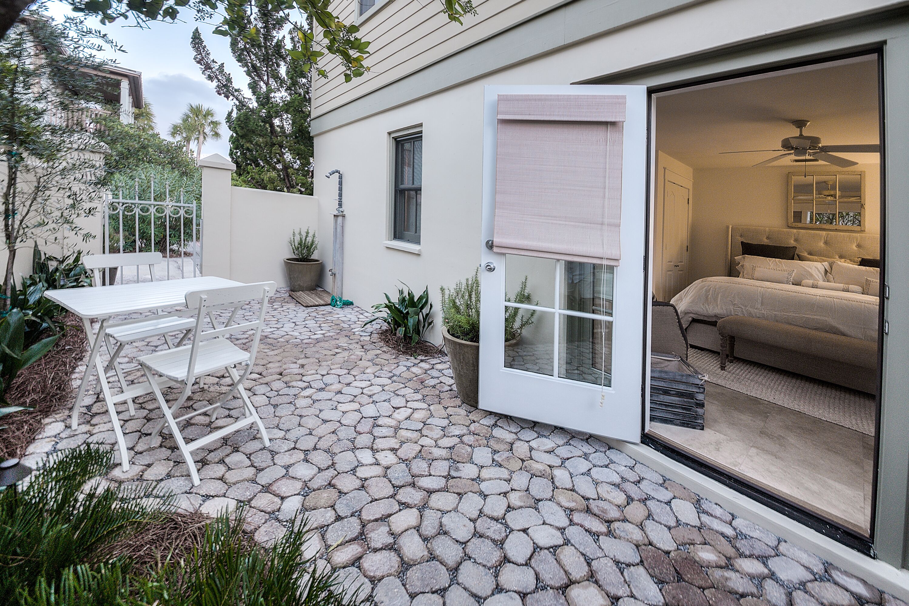 A patio with a stone floor, a white table and chairs, and a bedroom visible through an open door.