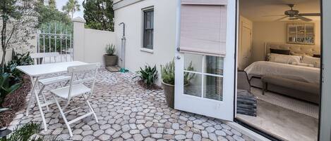 A patio with a stone floor, a white table and chairs, and a bedroom visible through an open door.