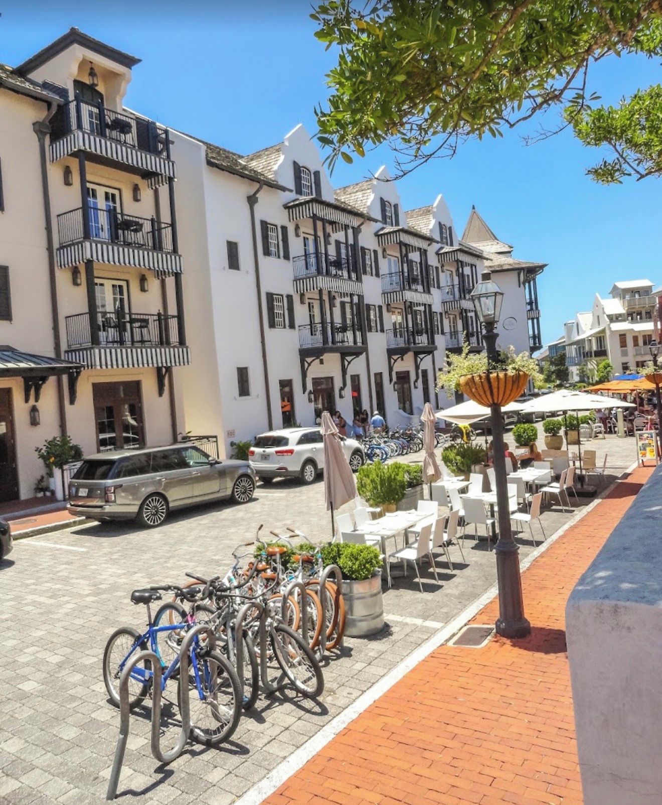 Una hilera de edificios de varios pisos con balcones, una calle pavimentada, bicicletas estacionadas y terrazas al aire libre.