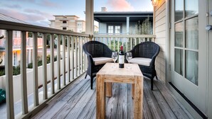 A wooden deck with two wicker chairs and a table, a bottle of wine, and two glasses.