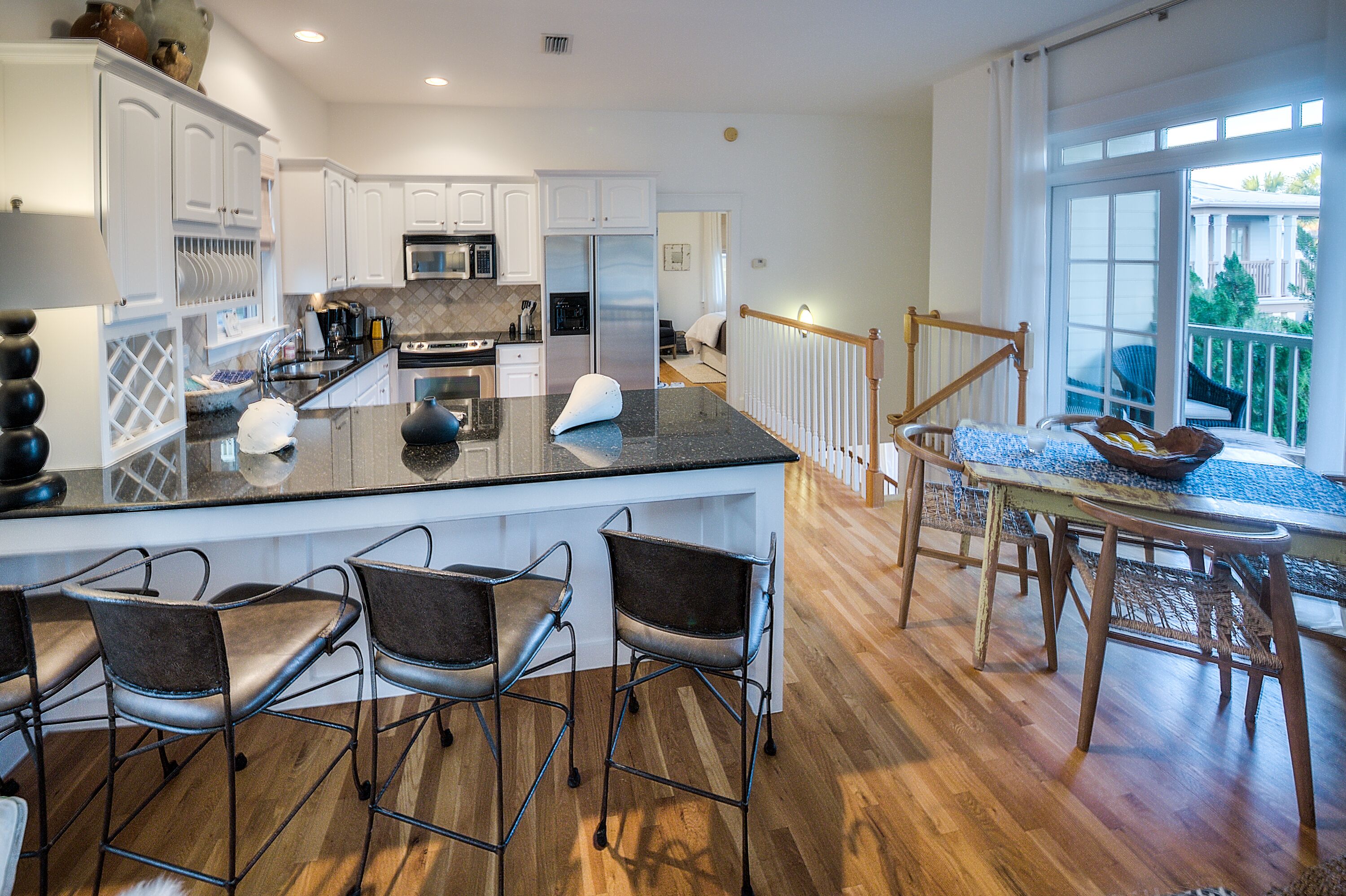 A modern kitchen with white cabinets, a central island with bar stools, and a dining area with a table and chairs.