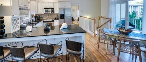 A modern kitchen with white cabinets, a central island with bar stools, and a dining area with a table and chairs.