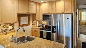 A modern kitchen with granite countertops, stainless steel appliances, and wooden cabinets. - Incredible Ocean View,  Most Desirable Unit in the Complex (Kihei)