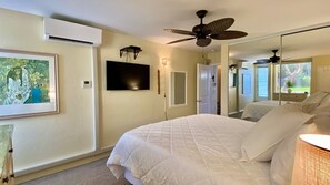 A bedroom with a large bed, a ceiling fan, a flat-screen TV, and a mirror. - Incredible Ocean View,  Most Desirable Unit in the Complex (Kihei)