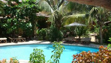 A pool area with a wooden deck, lounge chairs, and a thatched roof structure.