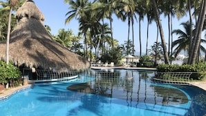 A swimming pool with a thatched roof structure, surrounded by palm trees and lounge chairs. - Marina Villas - Grand Isla Navidad (Isla Navidad)