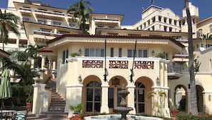 A courtyard with a fountain, palm trees, and a building with multiple balconies and arched windows. - Marina Villas - Grand Isla Navidad (Isla Navidad)