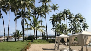 A beach with palm trees, a sandy path, and beach chairs under tents. - Marina Villas - Grand Isla Navidad (Isla Navidad)