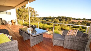 Une terrasse extérieure couverte, aménagée avec des meubles en osier, une table à plateau de verre et offrant une vue sur un paysage rural.
