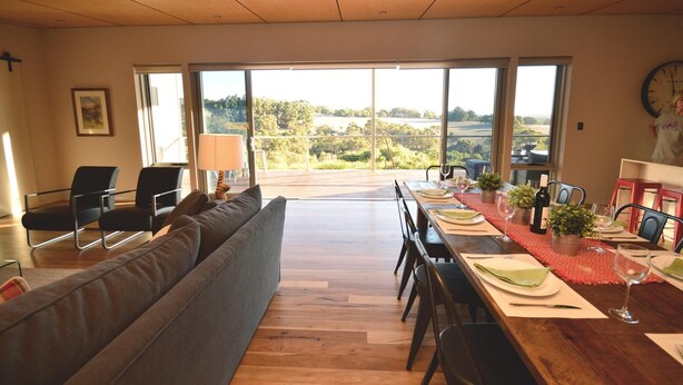 Un coin repas avec une table en bois dressée pour quatre personnes, un canapé et une vue sur l’extérieur.