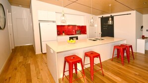 Une cuisine moderne avec des meubles blancs, un pare-feu rouge et un îlot central doté de tabourets.