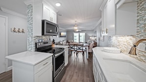 A modern kitchen with white cabinetry, a built-in microwave, and a dining area with a table and chairs. - Top-floor ocean view 2/2 with a balcony, heated beachfront pool, and beach access (New Smyrna Beach)