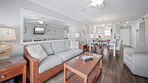 A modern living room with a grey sofa, a coffee table, and a dining area with a white table and chairs. - Top-floor ocean view 2/2 with a balcony, heated beachfront pool, and beach access (New Smyrna Beach)