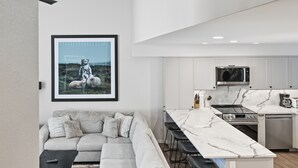 A modern kitchen with a large island, white cabinets, and a stainless steel microwave. - Newly renovated townhouse - bike right to your door, Private hot tub, BBQ (Silver Star Mountain)