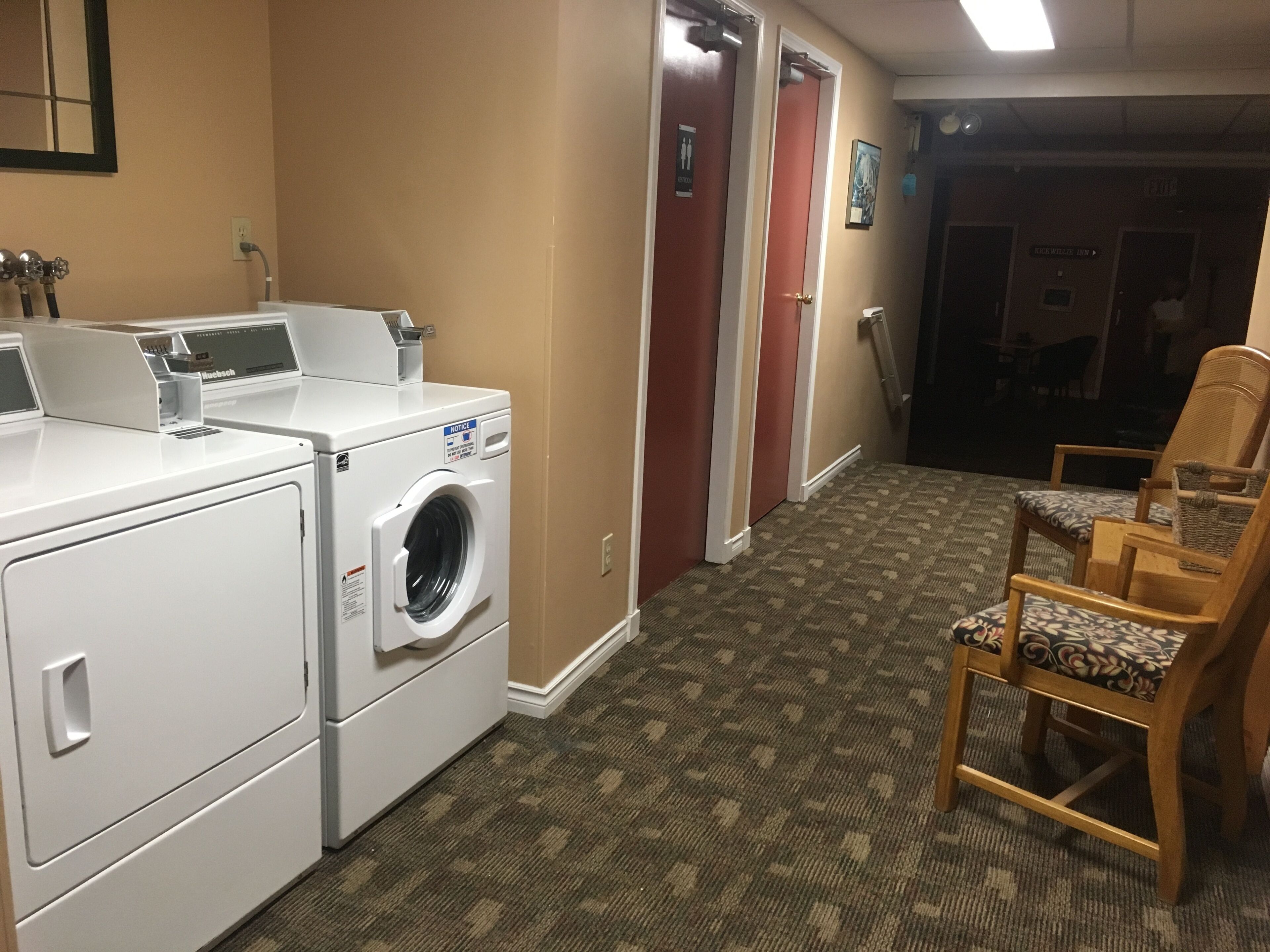 A laundry room with a front-loading washer and dryer, a wooden chair, and a carpeted floor.