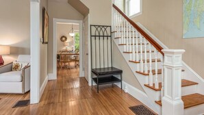 Eine Treppe mit weißen Balustern, ein Essbereich mit Holzsesseln und einem Tisch sowie ein Flur mit einem weißen Sofa.