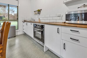 A modern kitchen with white cabinetry, a built-in oven, a microwave, and a window providing a view of the outdoors. - Woongara Cottage: Self-contained cottages on its own private acre (Eagle Point)