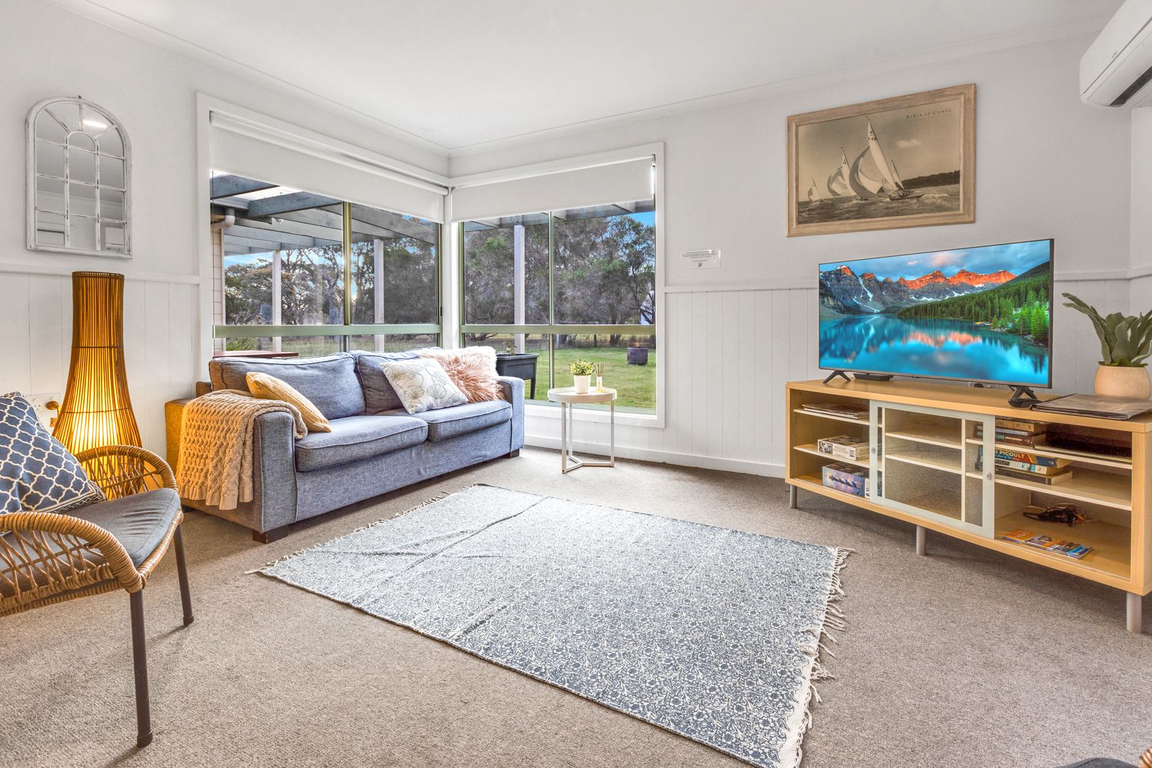 A living room with a sofa, a television, a bookshelf, and a large window offering a view of the outdoors.