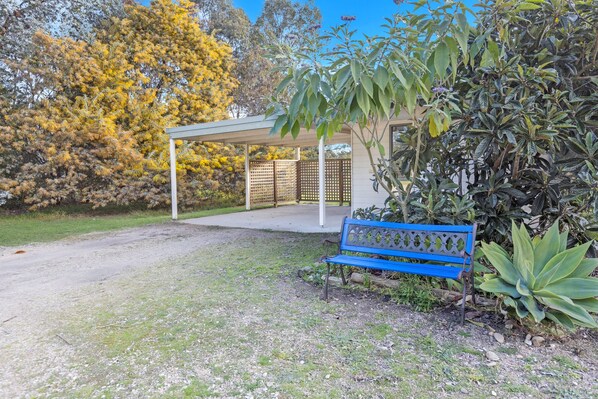 A covered outdoor seating area with a bench, surrounded by trees and plants. - Woongara Cottage: Self-contained cottages on its own private acre (Eagle Point)