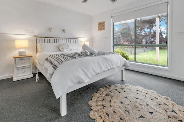 A bedroom with a bed, bedside tables, a lamp, a window, and a woven rug.