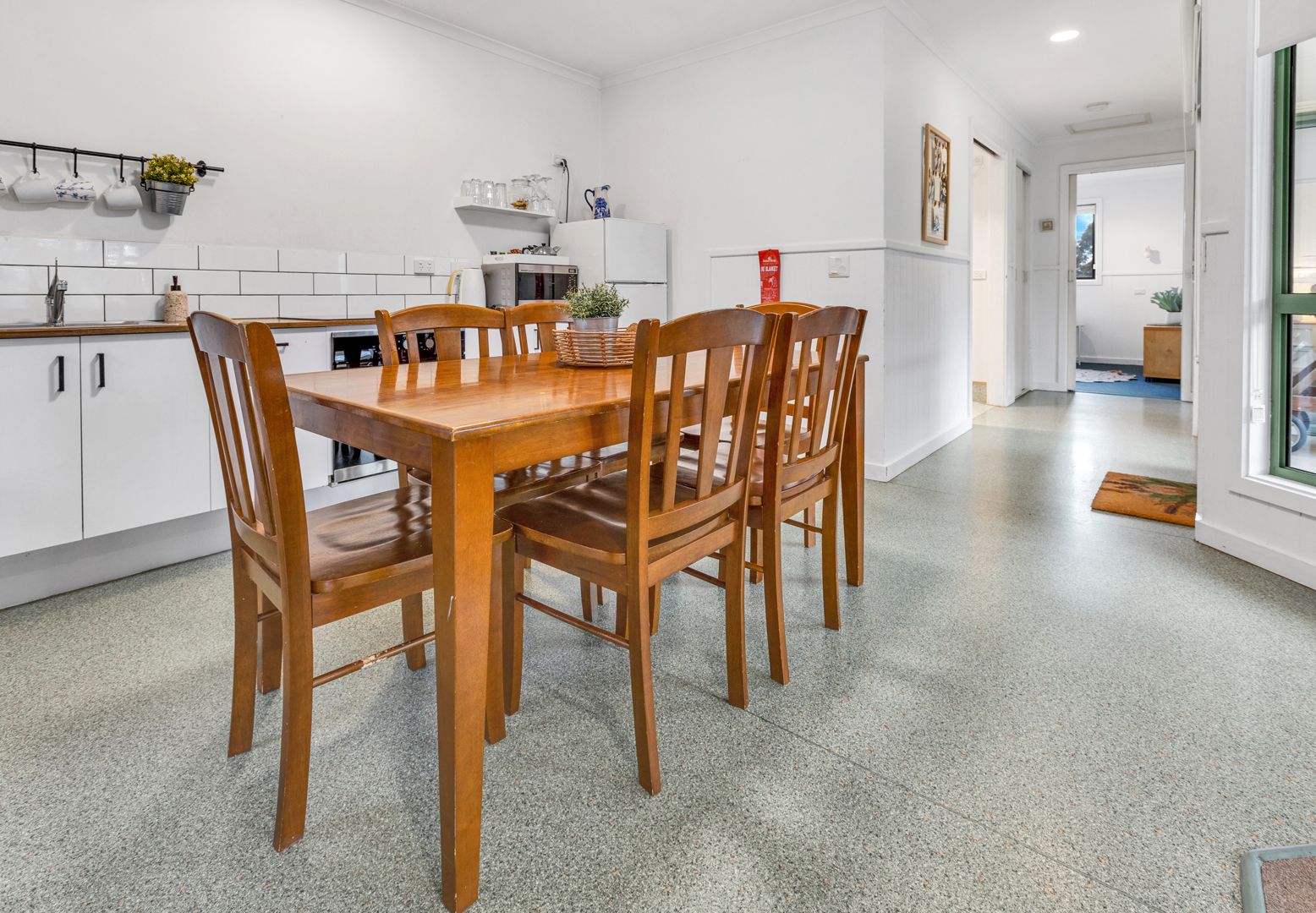 Una cocina moderna con armarios blancos, una mesa de comedor de madera y cuatro sillas.
