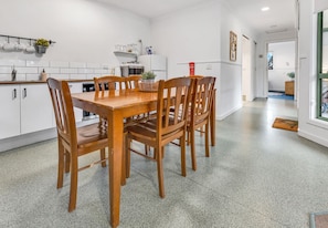 A modern kitchen with white cabinets, a wooden dining table, and four chairs. - Woongara Cottage: Self-contained cottages on its own private acre (Eagle Point)