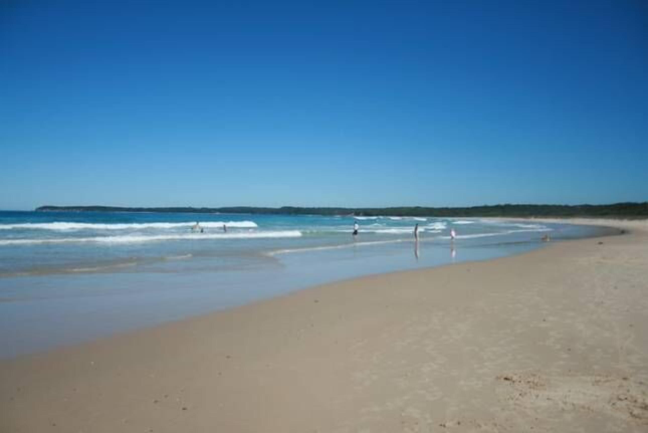 Una playa con cielo despejado, mar tranquilo y orilla arenosa.